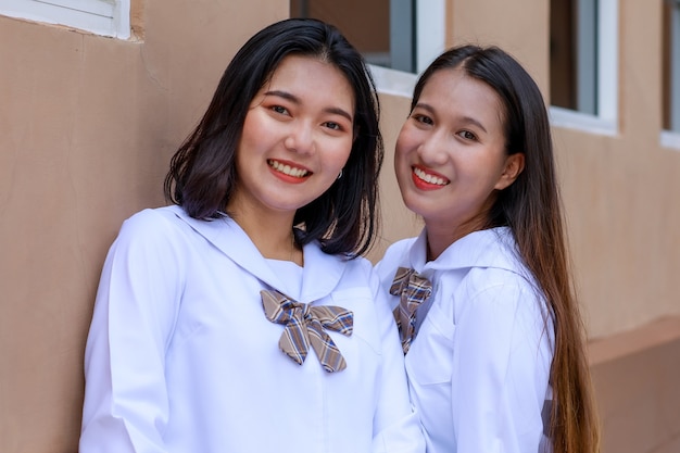 Leuke en jonge meisjes in Japanse, Koreaanse stijl schoolmeisjesuniform poseren voor de camera samen met plezier en blij voor het schoolgebouw. Goede vrienden in universiteitsconcept.