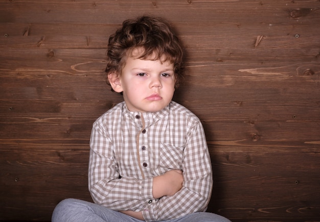 Leuke Europese jongen met krullend haar met een emotie van wrok op de achtergrond van een houten muur