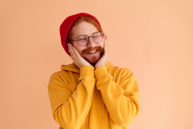Leuke foto van een knappe jongeman die lacht met zijn ogen dicht en een gele hoodiebril en een rode hoed draagt