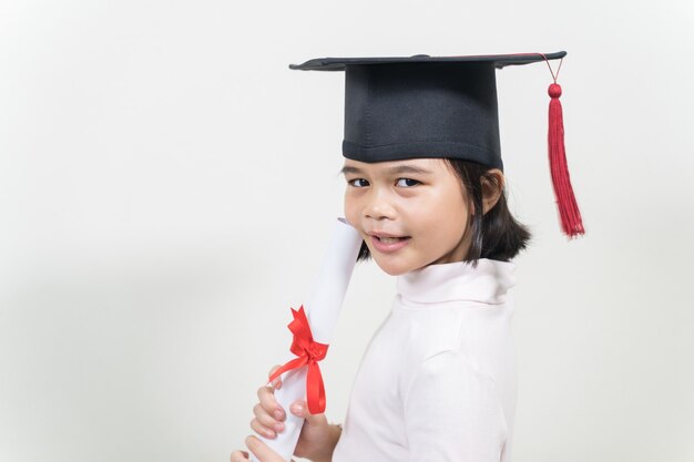 Leuke gelukkige aziatische schooljongen afgestudeerd met afstudeerhoed en een diploma geïsoleerd op een witte achtergrond