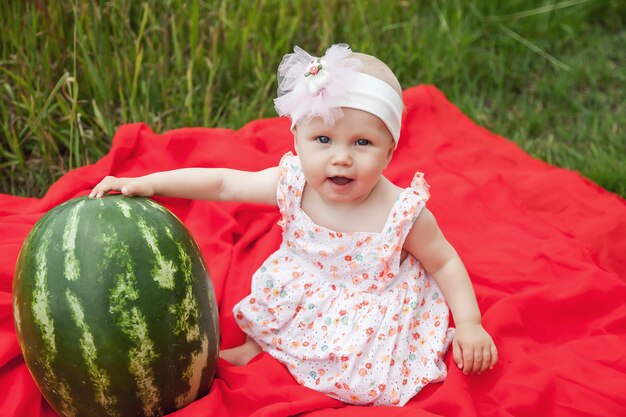 Leuke gelukkige blonde met blauwe ogen meisje 8 maanden in gras met watermeloen. concept van gezond eten, jeugd, fruitrijpheid, ouderschap, seizoensgebonden oogst. perfecte blanke baby in de zomer van de natuur