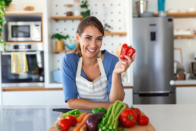 Leuke gelukkige jonge brunette vrouw in goed humeur een verse veganistische salade voorbereiden op een gezond leven in de keuken van haar huis