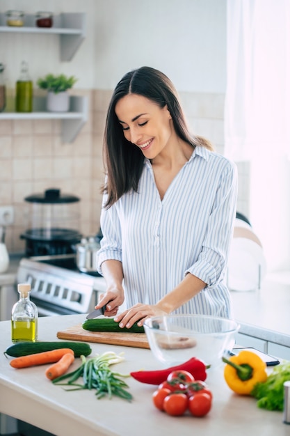 Leuke gelukkige jonge brunette vrouw in goed humeur een verse veganistische salade voorbereiden op een gezond leven in de keuken van haar huis