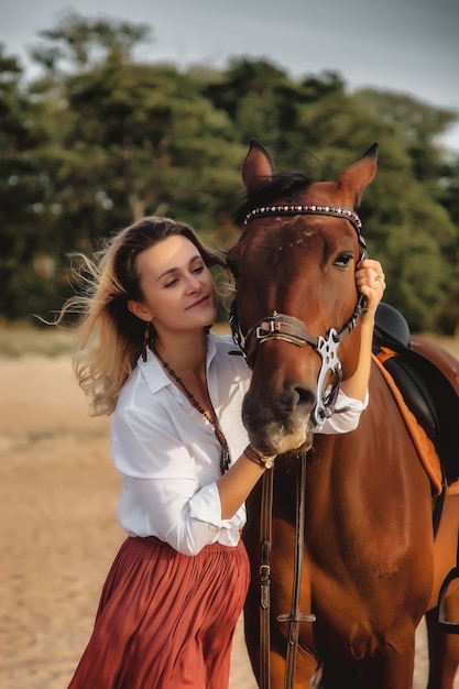 Leuke gelukkige jonge vrouw met paard in de zomer strand over zee. Rider vrouw rijdt haar paard in de natuur op avond zonsondergang lichte achtergrond. Concept van buiten rijden, sport en recreatie. Ruimte kopiëren