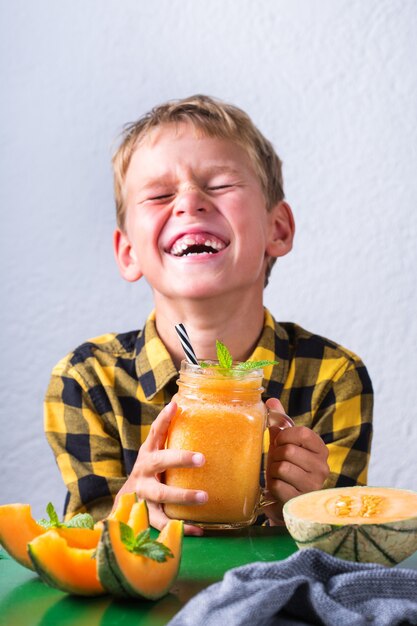 Leuke gelukkige jongen die gezonde meloen-smoothie drinkt