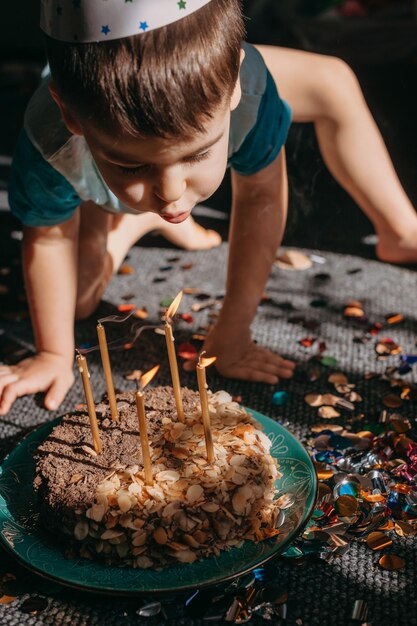Leuke gelukkige kleine jongen die brandende kaarsen blaast op zijn verjaardagstaartfeestje