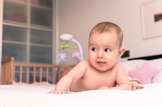 Leuke gelukkige lachende baby na bad het spelen op wit bed met hoofdkussens in zonnige jonge geitjesruimte.