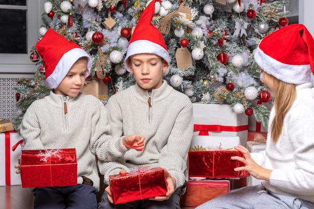 Leuke gelukkige opgewonden kinderen jongen en meisje in kerstmutsen pakken kerstcadeaudoos uit in mooie kamer