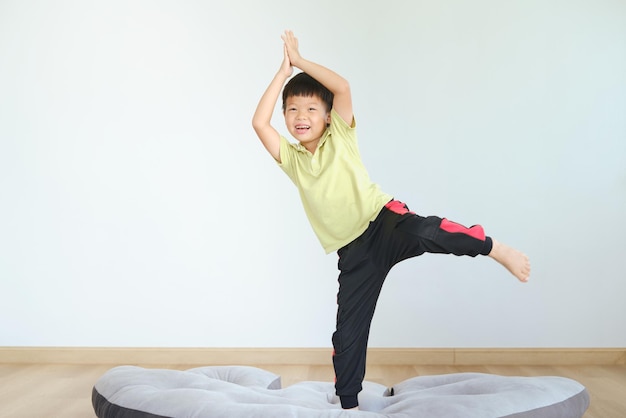 Leuke grappige Aziatische 5 jaar oude kleuterschool jongenskind probeert yoga in Tree Pose te beoefenen en binnen thuis te mediteren Gezonde levensstijl Yoga voor kinderen om de concentratie geïsoleerd op wit te verbeteren