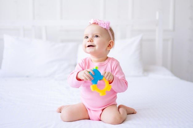 Leuke grappige jongen in roze bodysuit zittend met een rammelaar thuis op een bed met wit linnen bovenaanzicht Portret van een gezond kind