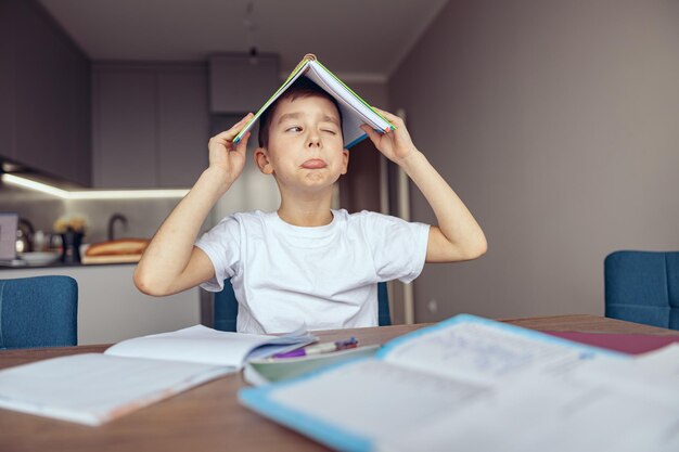 Leuke grappige kleine blanke tiener schooljongen die boek boven het hoofd houdt en lui huiswerk bespot