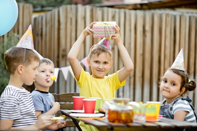 Foto leuke grappige negenjarige jongen die zijn verjaardag viert met familie of vrienden in een achtertuin verjaardagsfeestje kid draagt feesthoed en houdt geschenkdoos vast