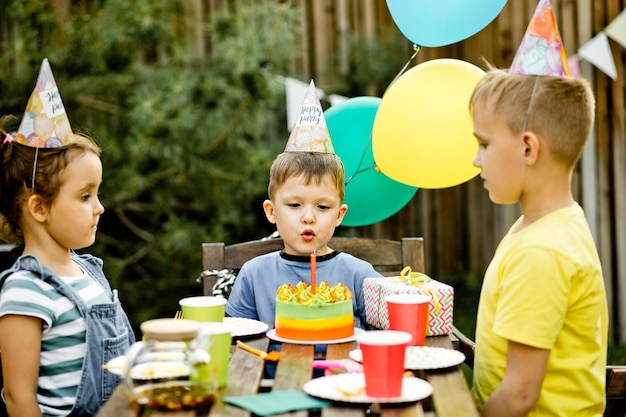 Leuke grappige vierjarige jongen die zijn verjaardag viert met familie of vrienden die kaarsen blazen op zelfgemaakte gebakken cake in een achtertuin verjaardagsfeestje voor kinderen