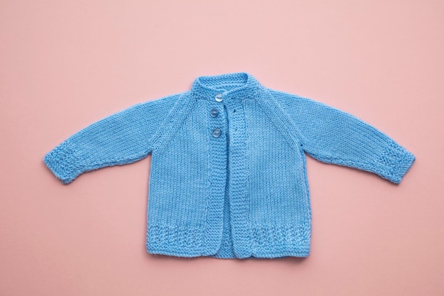 Leuke handgemaakte gebreide babykleding lay-out op een pastelroze achtergrond