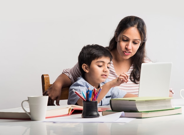 Leuke Indiase jongen met moeder die thuis huiswerk maakt met laptop en boeken - online scholingsconcept