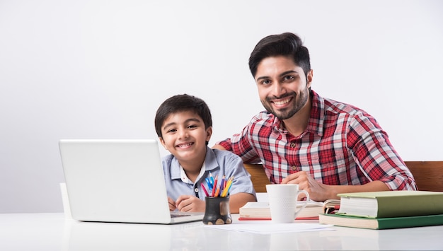 Leuke Indiase jongen met vader of mannelijke leraar die thuis huiswerk maakt met laptop en boeken - online scholingsconcept