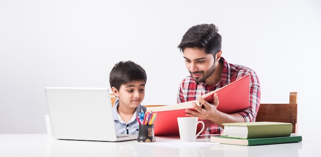 Leuke Indiase jongen met vader of mannelijke leraar die thuis huiswerk maakt met laptop en boeken - online scholingsconcept