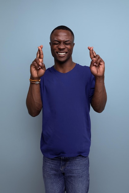 Leuke jonge Afrikaanse man in blauwe t-shirt gekruiste vingers op blauwe achtergrond