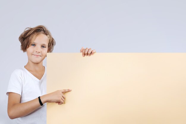Foto leuke jonge gelukkige jongen die leeg geel bord op wit houdt