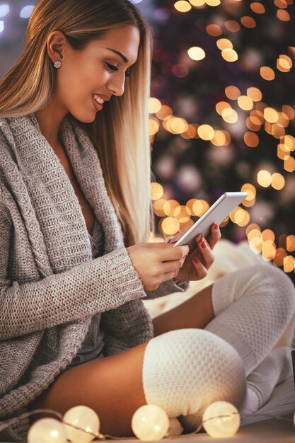 Leuke jonge glimlachende vrouw die smartphone gebruikt en glimlacht tijdens gezellige kerstvakanties thuis.