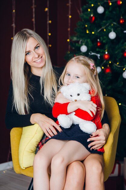 Leuke jonge moeder met blond haar en een dochtertje zitten op een stoel