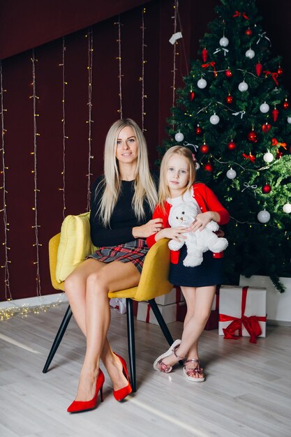 Leuke jonge moeder met blond haar en een dochtertje zitten op een stoel