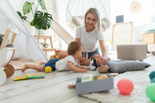 Leuke jonge moeder met haar kleine dochter spelen in de speelkamer met speelgoed Moederschap