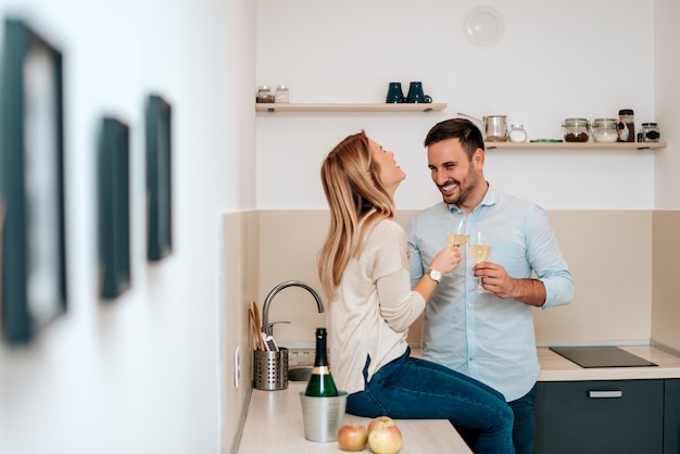 Leuke jonge paar het drinken wijn in keuken.