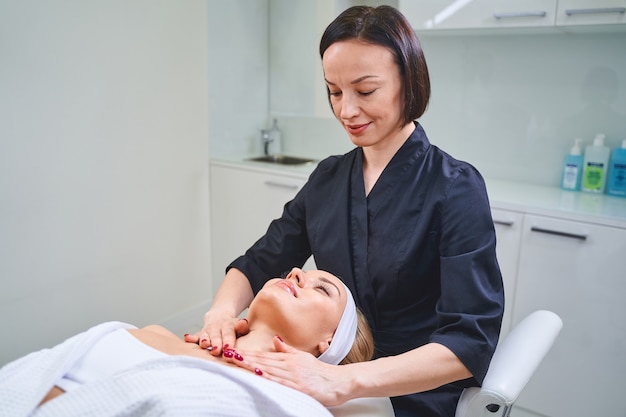 Leuke jonge vrouw die haar ogen gesloten houdt terwijl ze geniet van massage in de salon