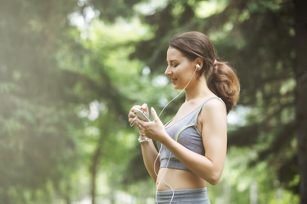 Leuke jonge vrouw die naar muziek luistert tijdens het joggen op het pad in een groen park