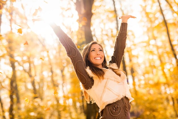 Leuke jonge vrouw die plezier heeft in het zonnige bos in herfstkleuren.