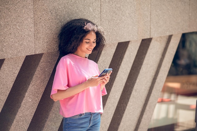 Leuke jonge vrouw die zich bij de muur met een telefoon in handen bevindt