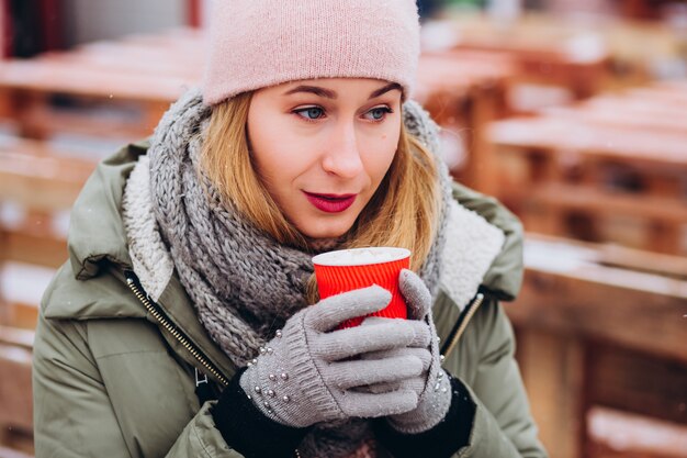 Leuke jonge vrouw hoed en roze trui dragen en warme chocolademelk drinken