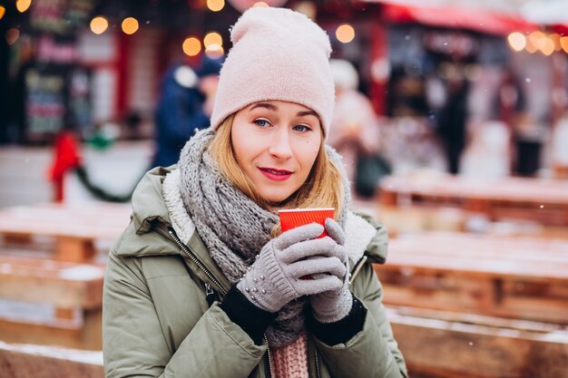 Leuke jonge vrouw hoed en roze trui dragen en warme chocolademelk drinken