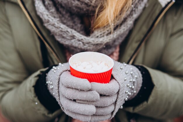 Leuke jonge vrouw hoed en roze trui dragen en warme chocolademelk drinken