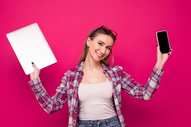 Leuke jonge vrouw in stijlvolle kleding met een telefoon en laptop op een roze achtergrond