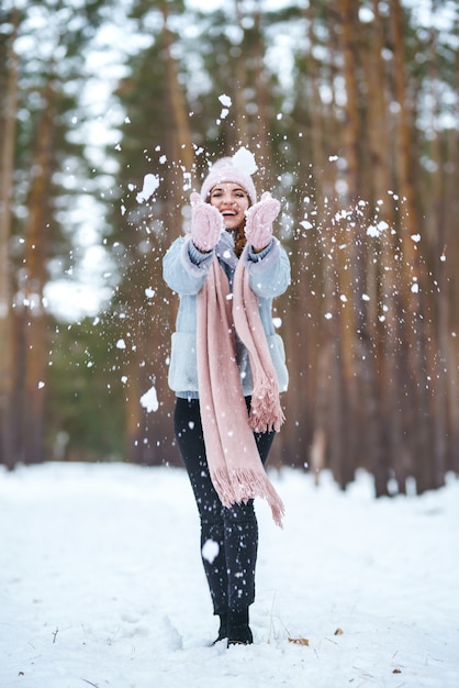 Leuke jonge vrouw speelt met sneeuw in het bos. Winter levensstijl geluk emoties natuur. Kerstmis, Nieuwjaar.