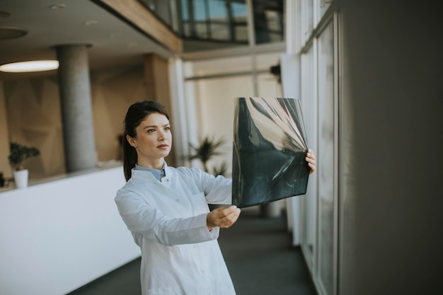 Leuke jonge vrouwelijke arts die röntgenfoto's op kantoor onderzoekt