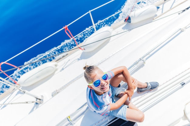 Leuke jongen aan boord van zeiljacht op zomercruise. Reisavontuur, zeilen met kind op familievakantie. Kinderkleding in zeemansstijl, nautische mode.