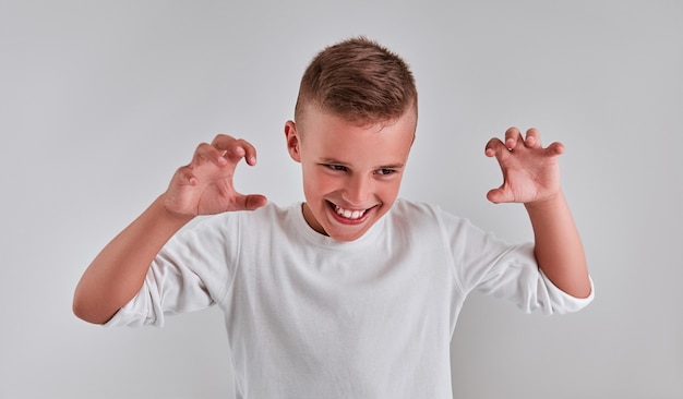 Foto leuke jongen die bang probeert te maken. emotioneel portret van een jongen op een grijze achtergrond. de jongen stak de handen van het monster uit.