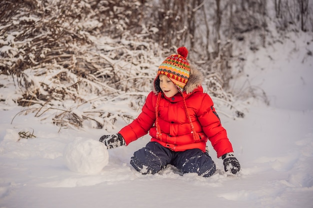 Leuke jongen die in rode de winterkleren een sneeuwman bouwt