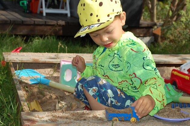 Foto leuke jongen die met speelgoed speelt terwijl hij op de speeltuin zit.