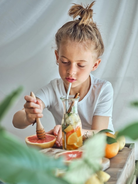 Leuke jongen die pomelo knijpt terwijl hij een gezond drankje maakt aan tafel met een fles vol gehakt fruit op een witte achtergrond in de kamer