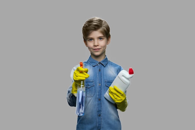 Leuke jongen die schoonmaakproducten houdt. Knap jong geitje dat in rubberhandschoenen fles met wasmiddel houdt. Home desinfectie. Lente schoonmaak concept.