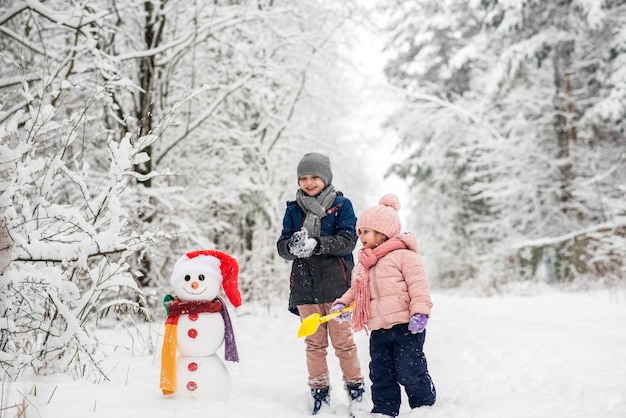 Leuke jongen en meisje sneeuwpop bouwen in winter wit bos