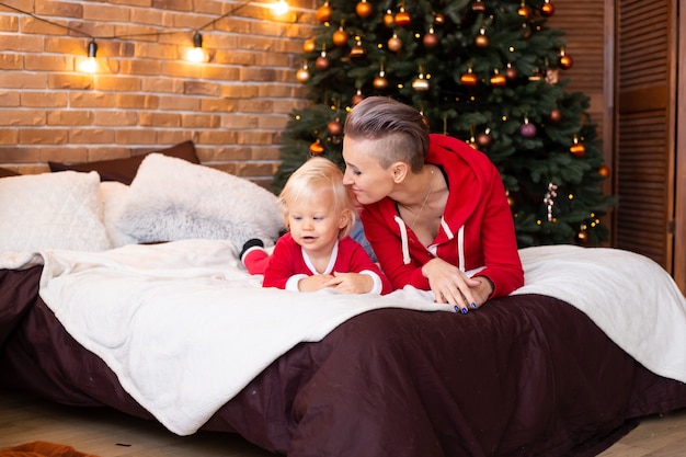 Leuke jongen en moeder op bed in de buurt van de kerstboom. kerstmis, vakantie en jeugdconcept