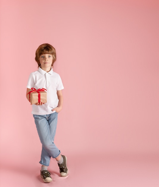 Leuke jongen houdt een geschenk in zijn handen op een roze achtergrond.