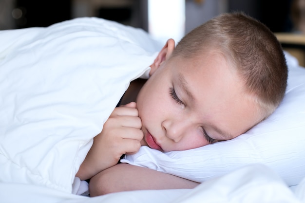 Leuke jongen in een wit bed onder een witte deken