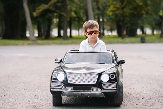 Leuke jongen in het berijden van een zwarte elektrische auto in het park