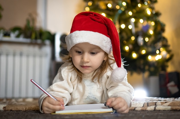 Leuke jongen in rode trui en rode kerstmuts schrijft een brief aan de kerstman